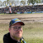 Andreas Duck als Marketing-Verantwortlicher mit Warnweste und Green Monster Cap beim Tractor Pulling Event in Füchtorf vor gut gefüllten Zuschauertribünen.