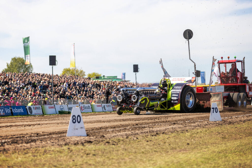 Rennaktion auf der Lehmbahn: Ein leistungsstarker Monster-Traktor des Green Monster Teams beschleunigt beim Tractor Pulling in Füchtorf vor Tausenden Zuschauern